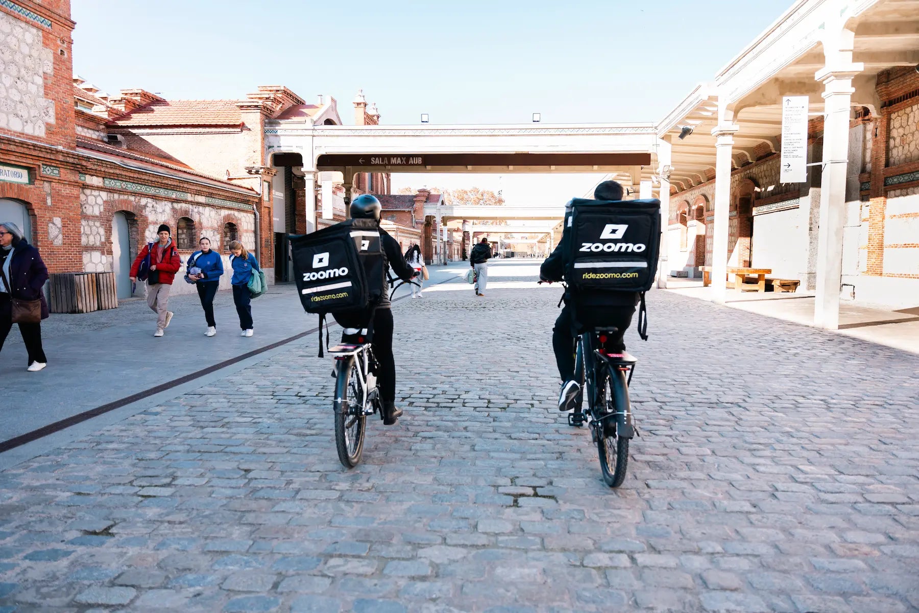 Two delivery riders cycling with their Zoomo e-bikes